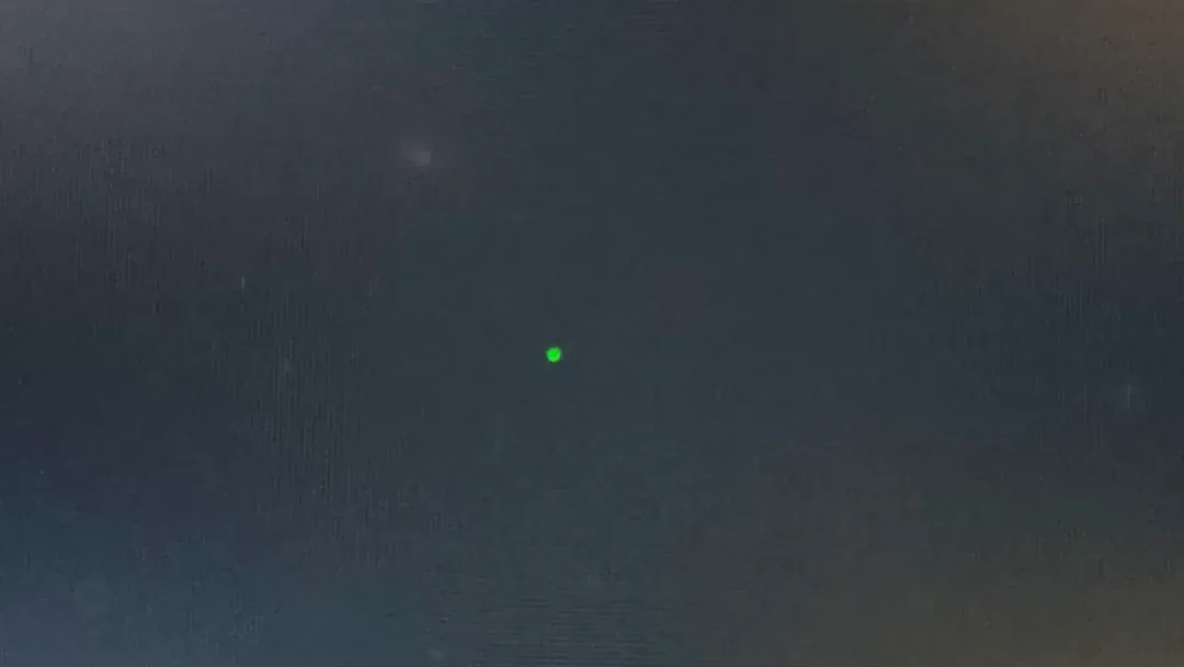 A single stuck pixel glowing green on a dark monitor, the surrounding pixels off